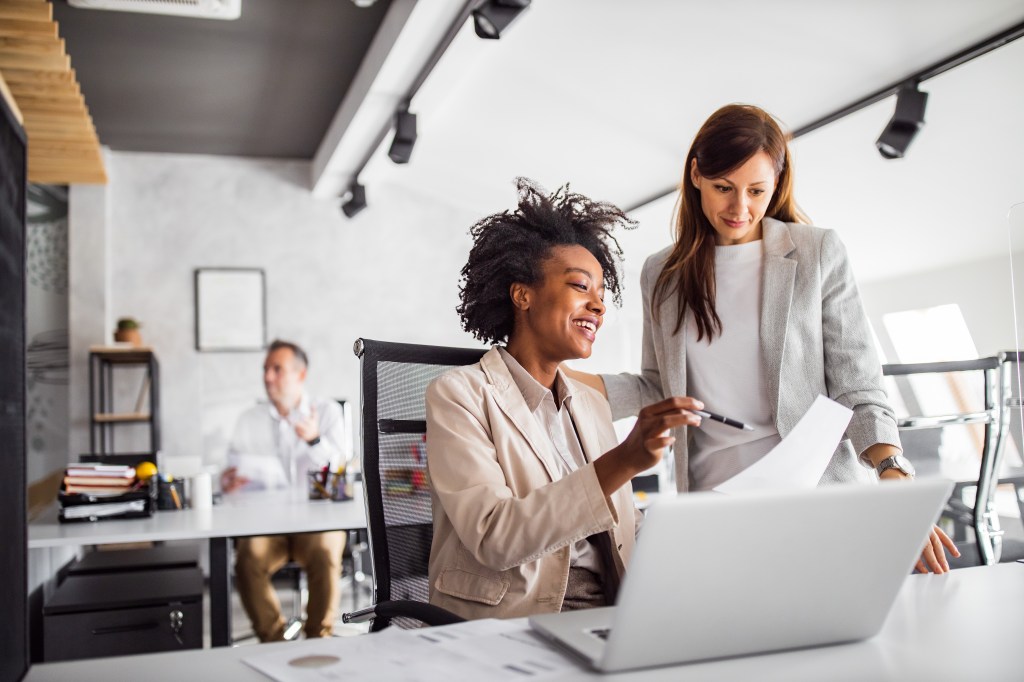 Two brunette business women, speaking, advising each other.