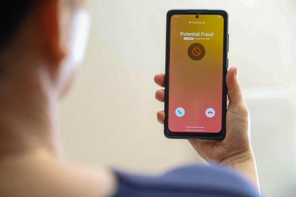 The hand holding a mobile phone by displaying an incoming call from an unknown caller, showing a possible spam call.