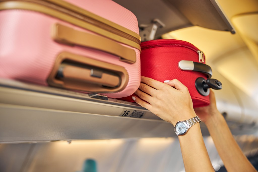 Hands of placement of carrier luggage on the upper bin on the plane.