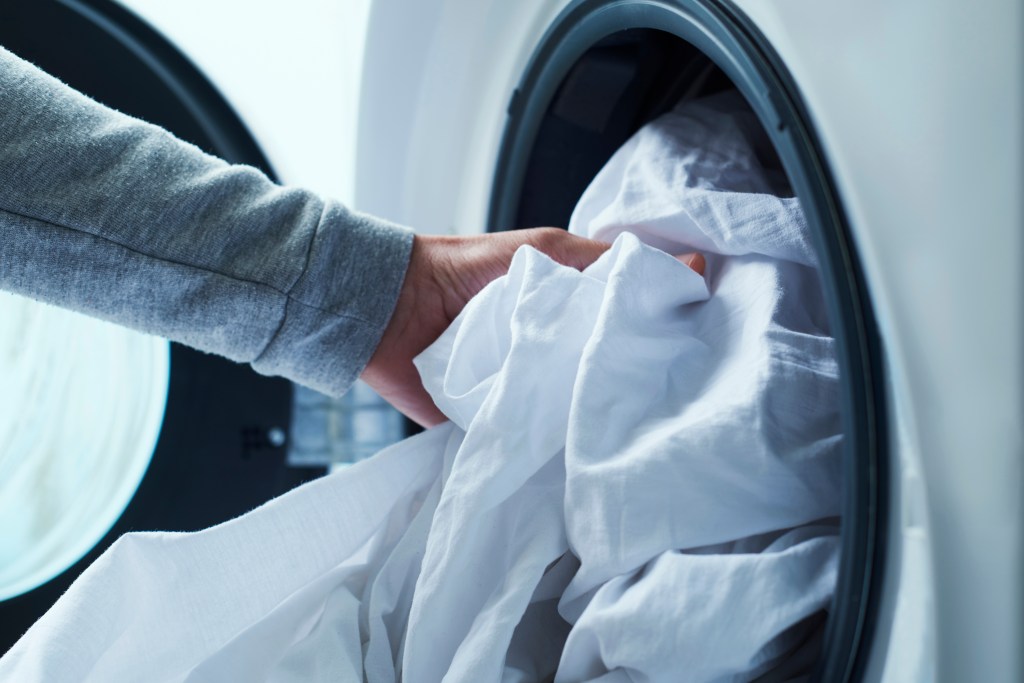 The person loading the white bed in a washing machine.