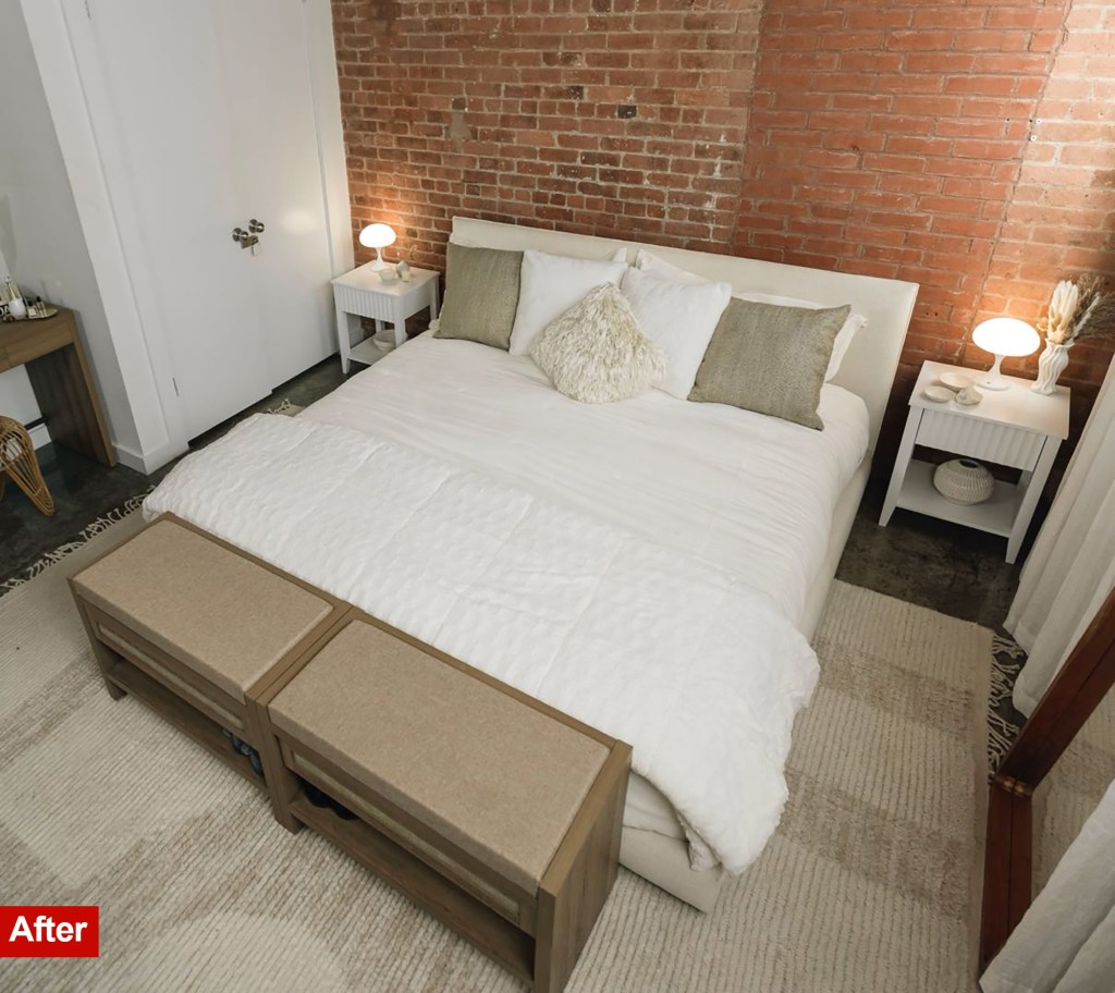 The bedroom makeover after: a white bed with beige pillows sits in a rug in front of a brick wall. Two matching benches are at the foot of the bed.