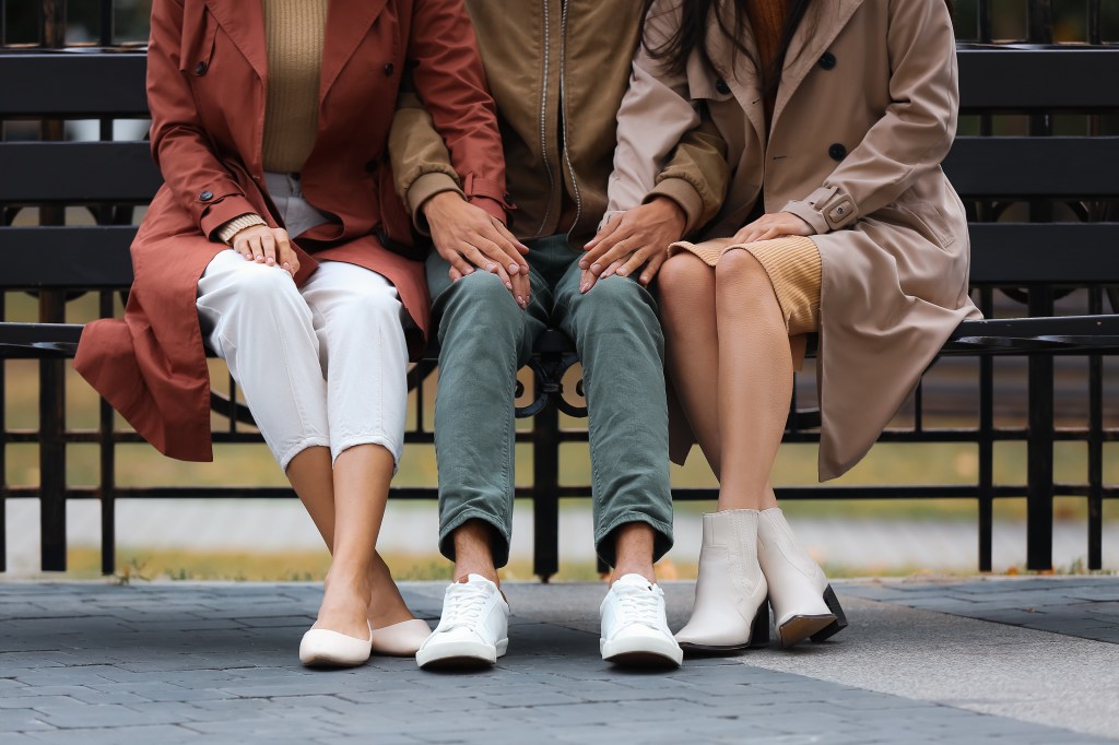 A man and two women sitting on a park bench, illustrating a polraramorus relationship.