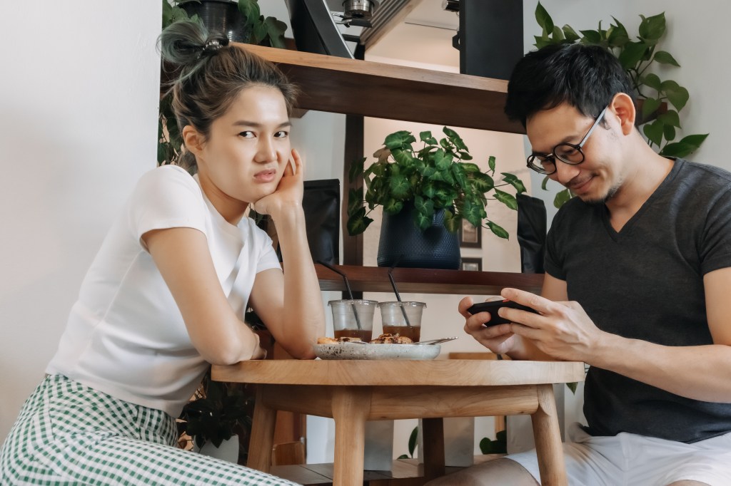 A woman looks bored while a man plays a removable game on a date.