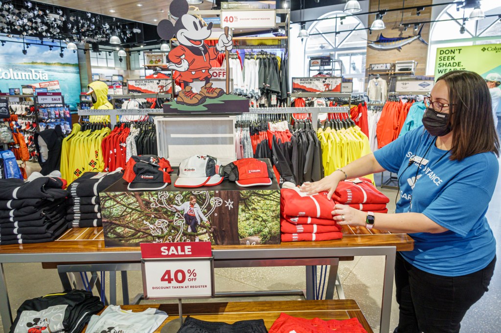 A retail worker dressed in a face mask arranges a performance of Columbia sportswear at a Walt Disney World store.