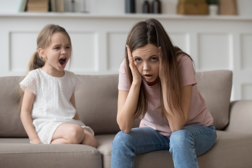 A stressed mother sits in a bed near her screaming daughter.