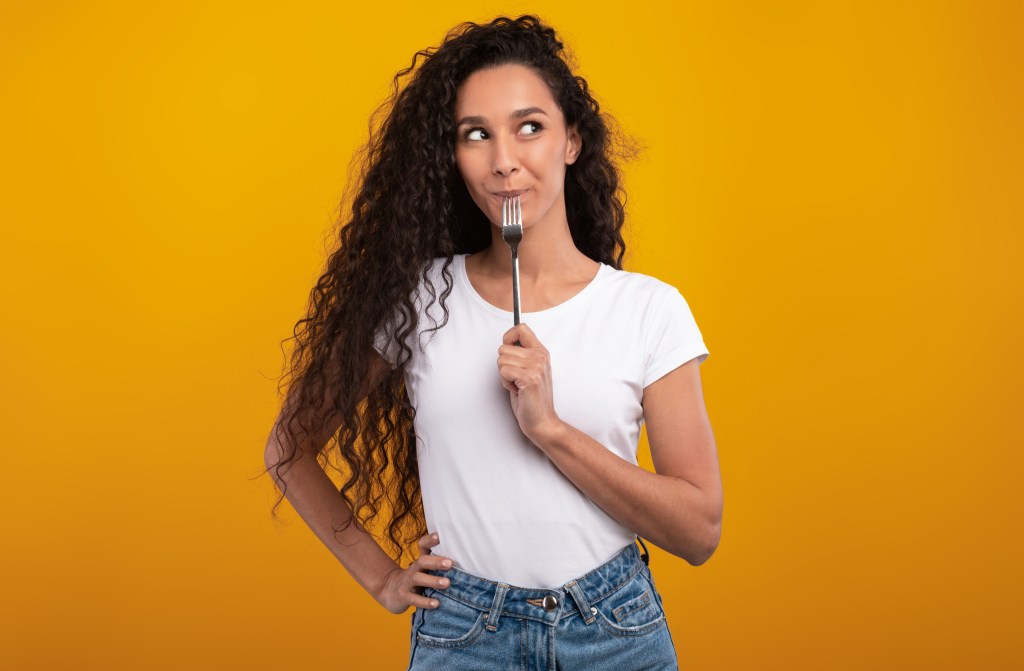 The woman holding a fork in her mouth, looking at the side on the side.